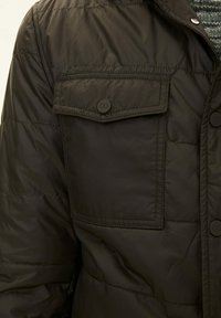Dark green puffer jacket with quilted design, buttoned flap pockets, and smooth texture. Features snap buttons and collar.