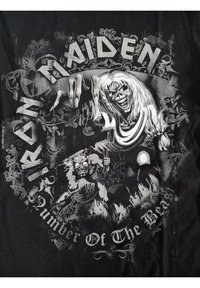 Černé tričko z bavlny s logem a grafikou Iron Maiden. Design zahrnuje kostlivce, plameny a složité vzory v bílé a šedé barvě.