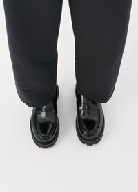 Sorte lædersko med en blank overflade, der har rund tå, tykk sål og en dekorativ rem hen over toppen.