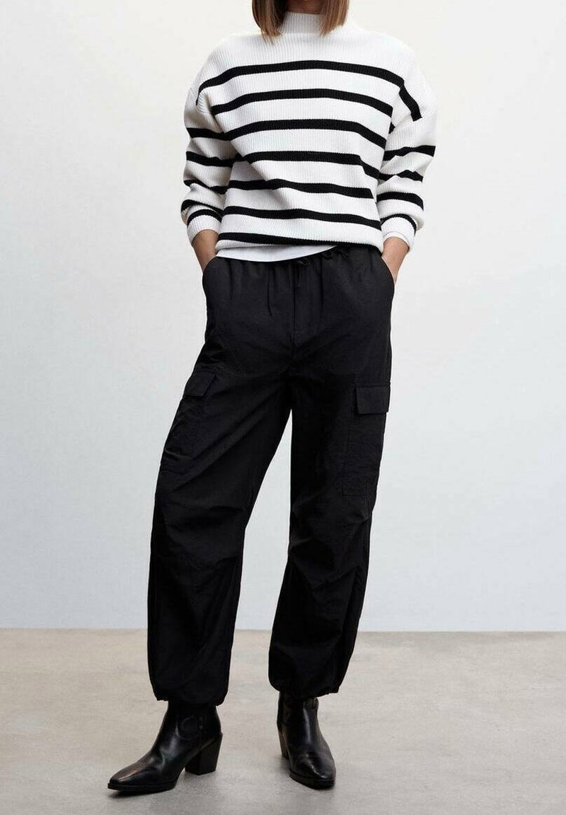 Pantalons cargo noirs avec poches latérales, associés à un pull en maille rayé noir et blanc. La tenue est complétée par des bottines noires.