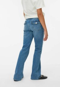 Jeans de mezclilla azul claro con un diseño de pierna acampanada, detalles en los bolsillos traseros y un acento de botón en la cintura. Textura suave, ajuste estándar.