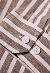Tela a rayas marrón y blanca con un tejido texturizado, que presenta dos botones blancos y un collar doblado.