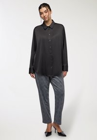 Camicia nera in satin con colletto, abbinata a pantaloni grigi a scacchi e scarpe con tacco nero.