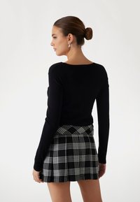 Schwarzer, taillierter Pullover mit langen Ärmeln, kombiniert mit einem karierten Rock in Schwarz und Weiß, der Falten und einen geraden Saum hat.