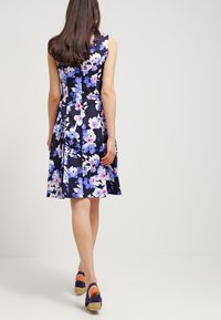 Vestido floral con fondo marino, con flores moradas y blancas, con un cuerpo ajustado, falda acampanada y diseño sin mangas.