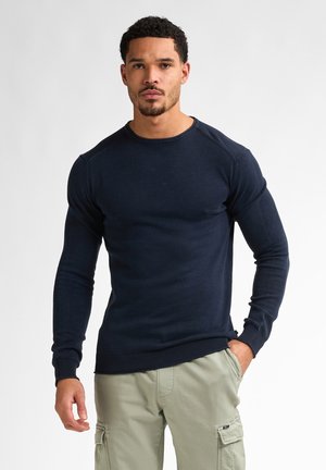 Suéter de punto en color navy, de manga larga y con cuello redondo, puños y dobladillo acanalados. Combinado con pantalones cargo de color caqui claro.