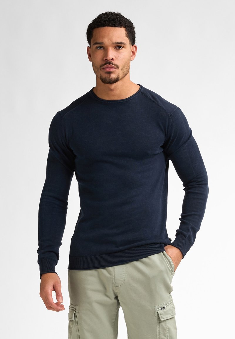 Mörkblå stickad långärmad tröja med rund halsringning, ribbade ärmslut och kant. Bärs med ljusa khaki cargo-byxor.