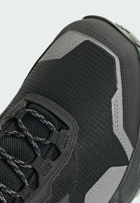 Sorte sportsko med struktureret mesh-overdel, slanke grå accenter og robust gummisål. Har metalhardware og forstærkede syninger.
