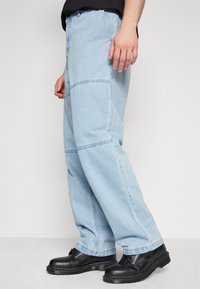 Jeans din denim albastru deschis, cu un croi lejer, având cusături vizibile și un design cu picior drept. Purtați cu botine negre cu șiret.
