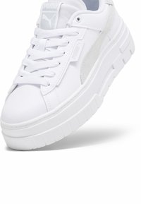 Zapatilla blanca con un upper de cuero suave, detalles en gamuza, lengüeta acolchada y suela gruesa con ranuras horizontales. Logo de Puma en los laterales.