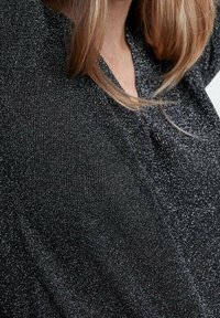 Top nero con texture e una leggera lucentezza metallica, caratterizzato da un collo a V e maniche corte. Il tessuto ha un aspetto morbido e liscio.