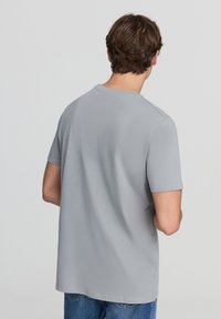 Jasnoszara, krótko rękawowa koszulka z okrągłym dekoltem i luźnym krojem, wykonana z gładkiego, miękkiego materiału. Czysty, minimalistyczny design bez widocznych logo.