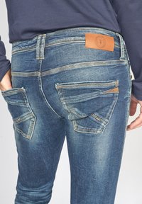 Denim jeans in vervaagd blauw met een rechte pasvorm, voorzien van twee achterzakken met schuine kleppen en een bruine leren label op de tailleband.