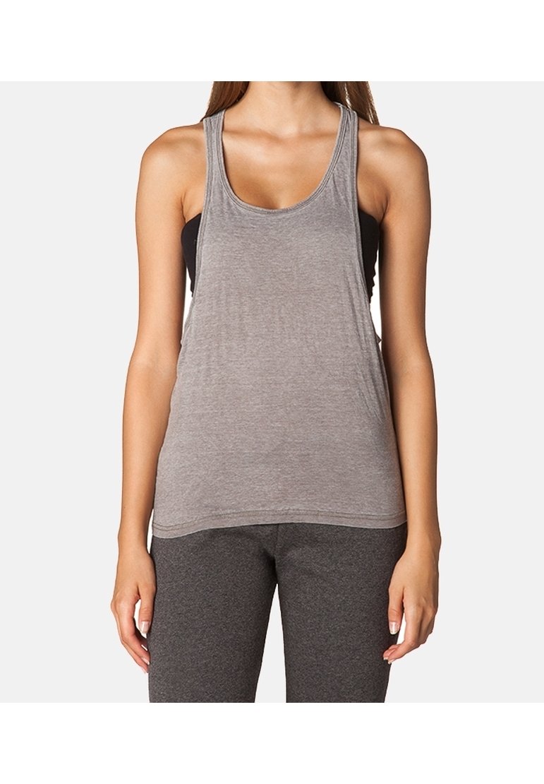 Femme portant un débardeur gris ample par-dessus un brassière de sport noire et des leggings gris foncé, debout devant un fond blanc uni.