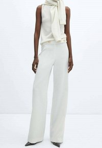Witte mouwloze top gelaagd met een lichte sjaal, gecombineerd met wijde witte broek met een knoopdetail in de tailleband.