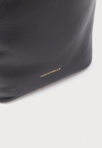 Zwarte leren handtas met een gladde textuur. Voorzien van een subtiel gouden logo, een minimalistisch ontwerp en een gestructureerde vorm.