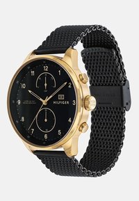 Montre analogique dorée avec un cadran noir et un bracelet en maille. Comprend deux sous-cadrans et un affichage de la date. Résistante à l'eau, au design épuré avec un boîtier en acier inoxydable.