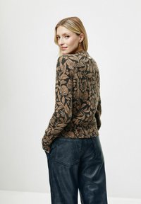 Brązowy sweter w kwiatowy wzór z ribbowaną teksturą, z długimi rękawami i okrągłym dekoltem. Nosi się go z ciemnymi, luźnymi spodniami.