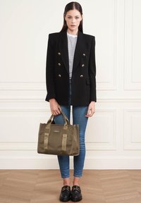 Blazer noir croisé avec des boutons dorés, chemise rayée, jeans skinny bleus, sac à main olive, et mocassins noirs avec des accents dorés.