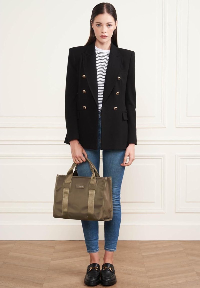 Blazer noir croisé avec des boutons dorés, chemise rayée, jeans skinny bleus, sac à main olive, et mocassins noirs avec des accents dorés.