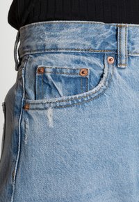 Ljust blå denimjeans med en urtvättad yta, utrustade med kopparnitar, en liten framficka och ett klassiskt midjeband.