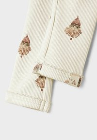 Żebrowany kremowy materiał; dwa rękawy z nadrukiem wzoru gnomów; miękka tekstura; mała metka marki na jednym rękawie.