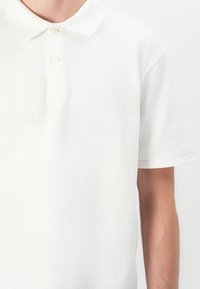 White polo shirt made of textured fabric, featuring a classic collar, two-button placket, and short sleeves.
