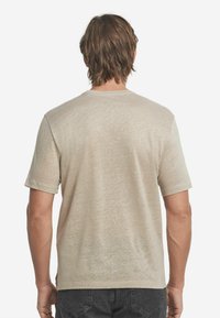 Beige t-shirt med kort ärm, tillverkad av ett lätt och texturerat tyg. Rund halsringning och rak passform med subtila detaljstickningar i fållen.