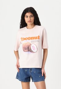 Lichtroze T-shirt met een "coconut" graphic in oranje, inclusief een tekening van een hele en een gehalveerde kokosnoot. Korte mouwen en een relaxte pasvorm.