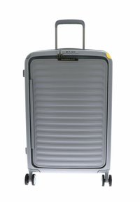 Valigia rigida grigia con texture a righe verticali, manico estraibile e accenti gialli. Presenta quattro ruote nere per la mobilità.