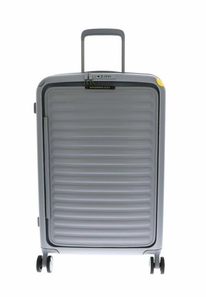 Valise rigide grise avec une texture à nervures verticales, poignée rétractable et accents jaunes. Comprend quatre roues noires pour la mobilité.