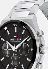 Montre en acier inoxydable avec un cadran noir et un motif texturé. Présente trois sous-cadrans, des index des heures argentés et une lunette polie. Résistance à l'eau jusqu'à 5ATM.