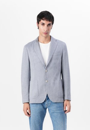 Blazer gris à carreaux avec revers crantés, deux boutons et poches avant, associé à un t-shirt blanc et un jeans bleu.