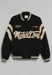 Schwarze Collegejacke mit beigen Akzenten, featuring das "Match Day" Logo in großer Kursivschrift, Druckknöpfen und gestreiftem Kragen und Bündchen.