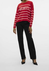 Pull rayé rouge avec des lignes blanches et un texte en script, associé à un pantalon noir et des escarpins noirs. Texture lisse, design décontracté.