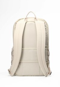Mochila de color beige claro con respaldo acolchado y correas ajustables, que presenta una textura de tela suave y un asa en la parte superior.