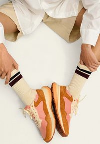 Zapatillas con ante rosa y beige, detalles en crema y una suela de goma texturizada, combinadas con calcetines de crema acanalados con rayas burdeos.