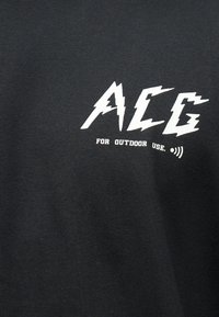 Μαύρο ύφασμα με άσπρο κείμενο "AEG" σε στιλιζαρισμένη γραμματοσειρά και μικρότερο κείμενο από κάτω που γράφει "FOR OUTDOOR USE." με ένα εικονίδιο σήματος.