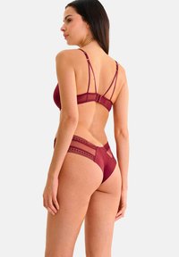Ensemble de lingerie bordeaux comprenant un soutien-gorge avec des accents en mesh transparent et un design à plusieurs bretelles, associé à un string assorti avec des détails en dentelle.