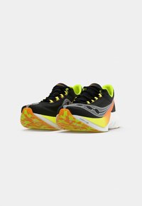Baskets de course noires avec des accents jaune fluo, partie supérieure texturée, semelle orange et blanche, détails réfléchissants, et un motif de semelle.