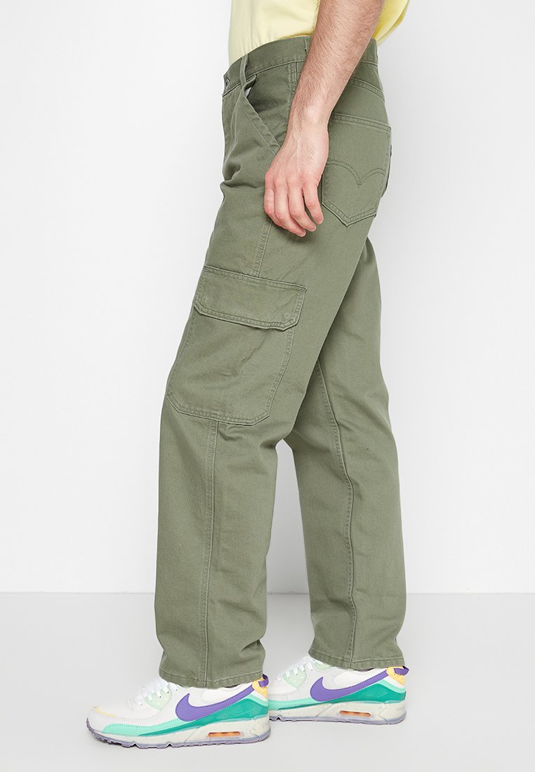 Pantalons cargo verts avec plusieurs poches, coupe droite, en coton et avec des coutures renforcées. Associés à des baskets blanches et colorées.