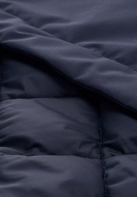 Loděnická modrá péřová bunda vyrobená z látky s hladkým vnějším povrchem a prošívanými částmi, které zdůrazňují izolační design a detaily šití.