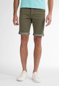 Shorts roulés vert olive avec une texture semblable au denim, présentant un revers intérieur vert clair contrastant et une étiquette rouge sur la poche arrière.