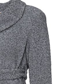 Cappotto grigio intrecciato con un motivo testurizzato, colletto ampio e una cintura coordinata in vita, che presenta un design sartoriale e strutturato.