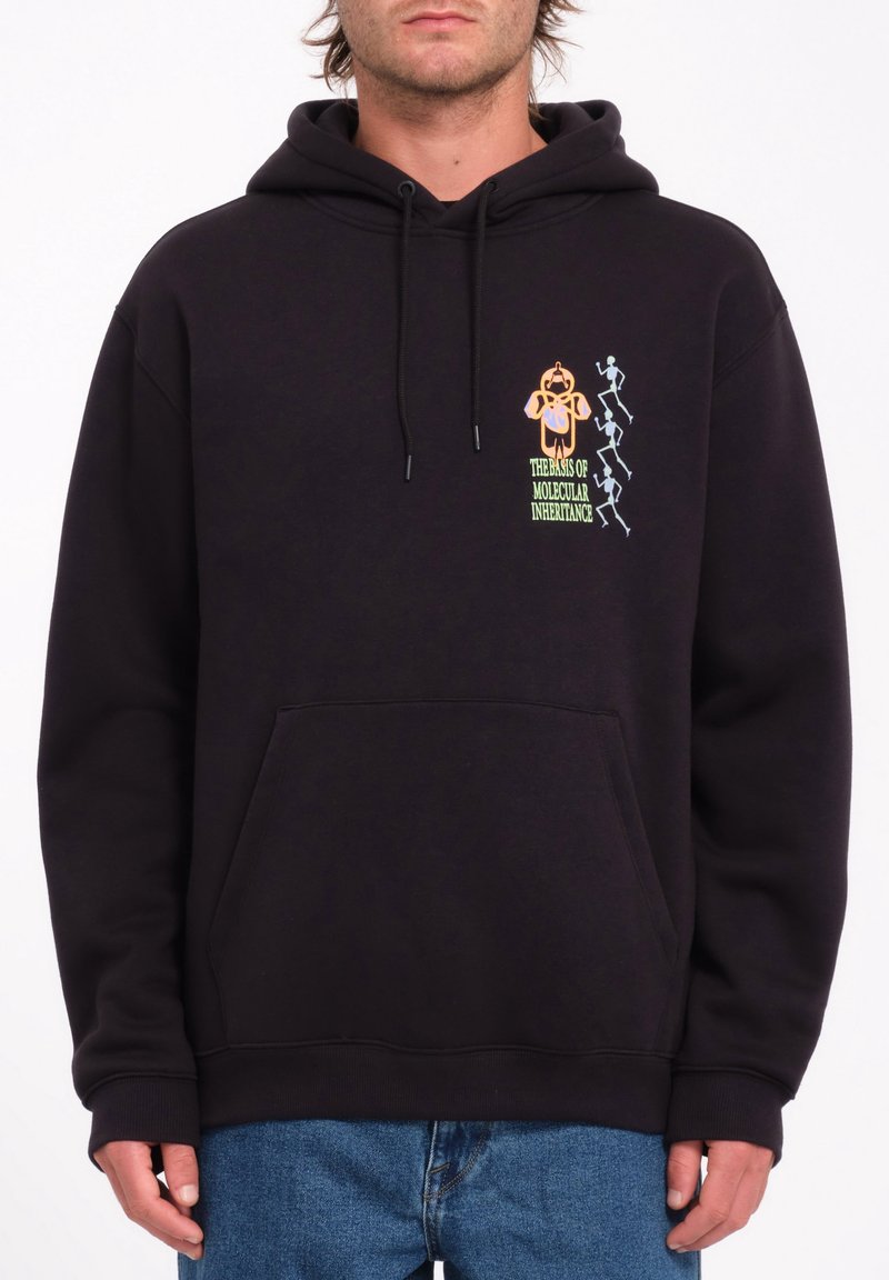 Homme portant un sweat à capuche noir avec un motif jaune et blanc de figures et le texte « The Basis of Molecular Inheritance » sur la poitrine.