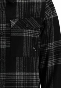 Camicia in flanella a scacchi nera e grigia con tasca frontale, chiusura a bottoni e texture liscia; presenta un pannello nero solido a contrasto.
