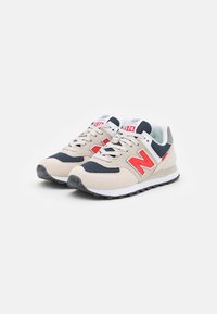 Beige und marineblaue Sportsneaker aus Mesh- und Wildledermaterialien, mit einem leuchtend roten "N"-Logo, weißer Sohle und neutralen Schnürsenkeln.