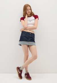 Top corto de manga corta rojo y blanco, falda mini de mezclilla oscura con dobladillo de mezclilla clara, combinada con zapatillas burdeos y calcetines grises.