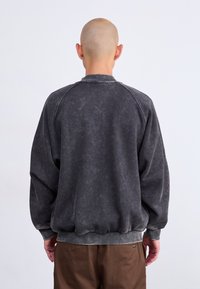 Sweatshirt cinza carvão com mangas raglan, punhos ribateados e cintura ribateada. Tecido suave e texturado com um acabamento levemente desbotado.