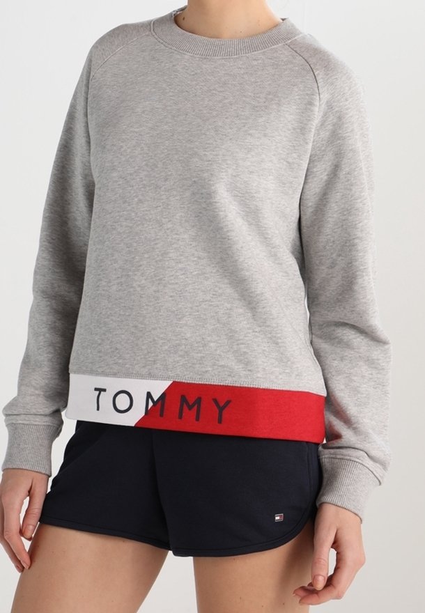 Šedá bavlněná mikina s ribovaným výstřihem a dlouhými rukávy, na spodním lemu s červenobílým pruhem, na kterém je nápis "TOMMY".
